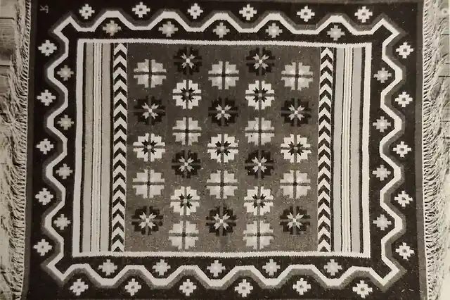 A whole flatweave in brown, cream and black with a stepped border and fringe at both ends, lying on wooden boards