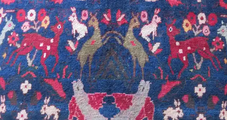 Blue wool pile with deer, rabbits and small flowers knotted in red, pink and white