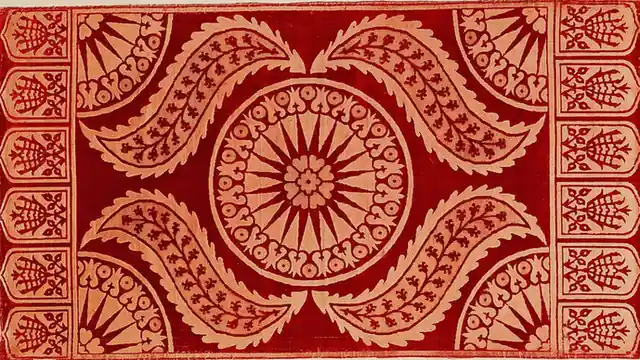 A cushion face in deep red and cream: a round medallion at the centre, curved leaves around it and a row of small arches down each end