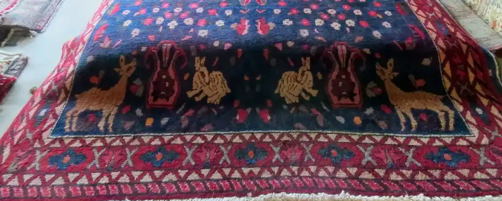 A blue-ground rug laid flat on the floor of the room, its lower border and fringe nearest the camera, other pieces at the edges