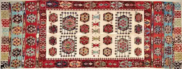 A long two-panel flatweave: hexagons on a cream field inside a red border of hooks
